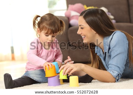 Happy mother and concentrated baby daughter playing with toys together sitting on the floor of the living room at home