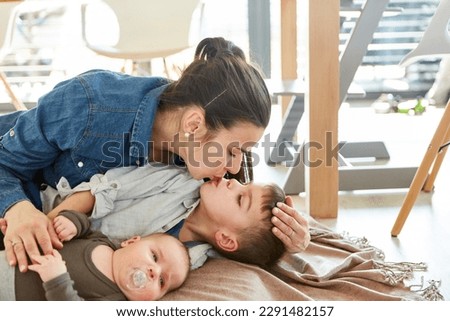 Happy mother cuddling with two children and giving big brother a loving kiss
