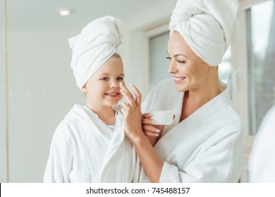 Happy Mother And Daughter In Bathrobes And Towels Applying Face Cream Together