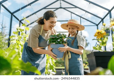 Happy mother and daughter are gardening in the greenhouse. Child is helping her mom and learning about botany. - Powered by Shutterstock