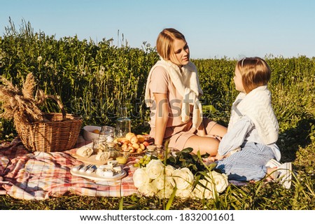 Happy mother and daughter have a rest together in a picnic outdoors. Blue pink clothes, casual.