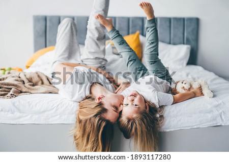 Happy mother and daughter having fun and playing together on the bed at home. 