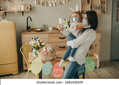 Happy mother with daughter in her arms making selfie on kitchen background and easter eggs and tulips home on quarantine with medical mask. Coronavirus, illness, infection, flue, surgical bandage. - Powered by Shutterstock