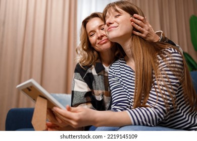 Happy Mother And Daughter Hugging While Sitting On Sofa And Looking At Framed Photo