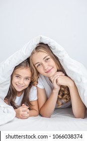 Happy mother with daughter lie on the bed under the blanket. Space for text