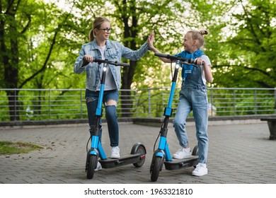 Happy mother and daughter making high five gesture before riding electric scooters in city park - Powered by Shutterstock