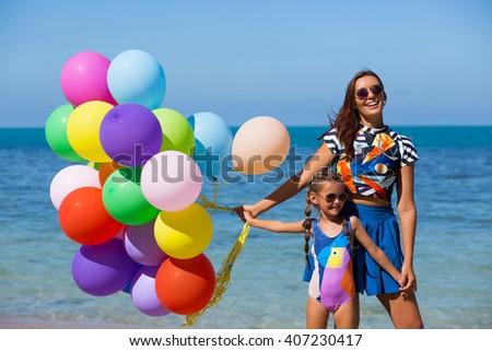 Happy mother and daughter on the beach, holding flying colorful balloons