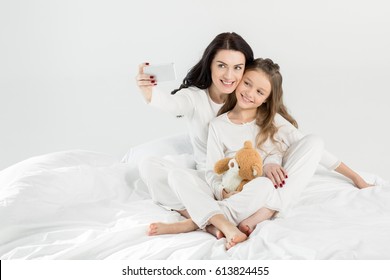 Happy mother and daughter in pajamas taking selfie with smartphone on bed isolated on white - Powered by Shutterstock