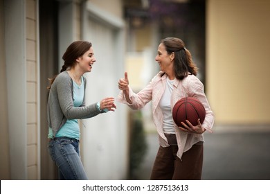 Happy Mother And Daughter Playing Basketball On Their Driveway.