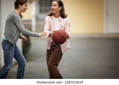 Happy Mother And Daughter Playing Basketball On Their Driveway.