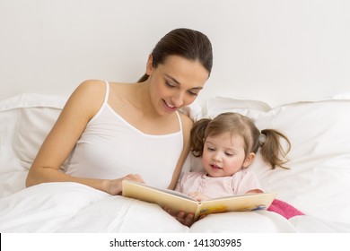 Happy mother and daughter reading a book together in bed