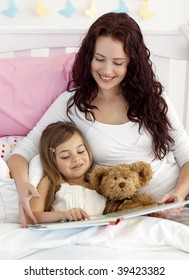 Happy Mother And Daughter Reading A Book Together In Bed