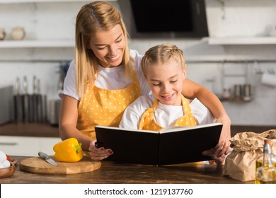 Happy Mother And Daughter Reading Cookbook While Cooking Together