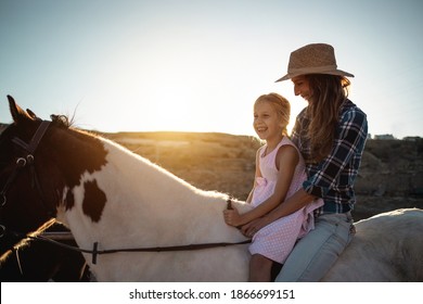 Happy mother and daughter riding a horse at sunset - Family and love concept - Focus on kid face - Powered by Shutterstock