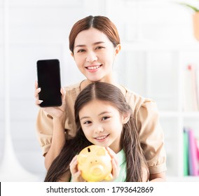 Happy Mother And Daughter Showing The Mobile Phone And Piggy Bank