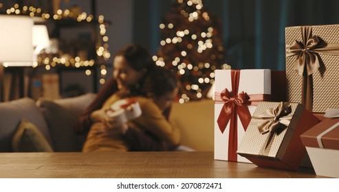 Happy mother and daughter sitting in the living room and exchanging gifts, Christmas presents in the foreground - Powered by Shutterstock