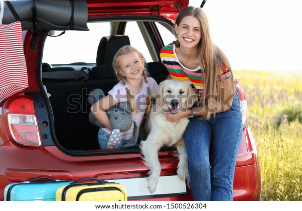 Happy mother and daughter with their dog in car
trunk outdoors