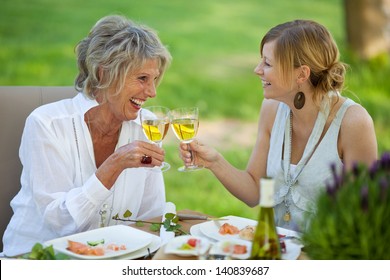 Happy mother and daughter toasting white wine at dining table in lawn - Powered by Shutterstock