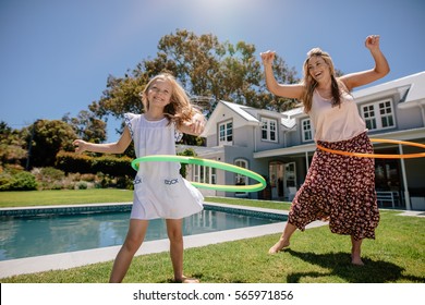 Happy Mother And Daughter Twirling Hula Hoops. Beautiful Young Woman And Little Girl Playing With Hula Hoop In Their Backyard.