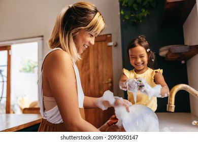 Happy mother and daughter washing dishes with bubbles. Mother and daughter having fun together in the kitchen. Loving single mother spending quality time with her young daughter at home. - Shutterstock ID 2093050147
