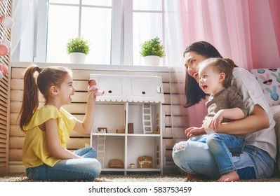 Happy mother and daughters girls play with doll house at home. Funny lovely family are having fun in kids room.