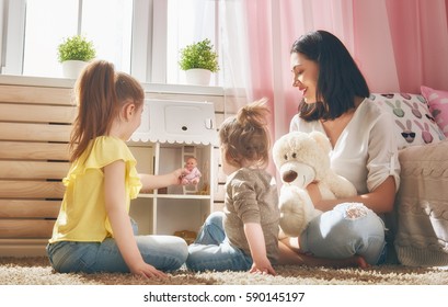 Happy mother and daughters girls play with doll house at home. Funny lovely family are having fun in kids room.
