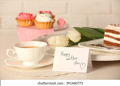 Happy mother day greeting with tulips, cup of tea and delicious cupcakes on wooden table closeup - Powered by Shutterstock