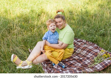 A Happy Mother And A Disabled Child Are Sitting On The Grass In The Park And Gently Hugging. Summer Holidays. Disability