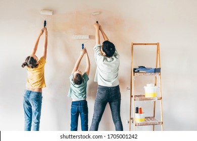 Fröhliche Mutter, Doppel und Sohn, die Mauer mit Rollen malte. Mama lehrt ihre Kinder, wie sie zuhause mit Rollen malen.