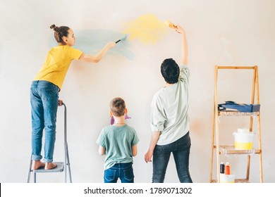 Happy Mother, Douther And Son Painting Wall With Roller. Mom Teachs Her Children Painting With Roller At Home.