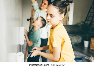 Happy Mother, Douther And Son Painting Wall With Roller. Mom Teachs Her Children Painting With Roller At Home.