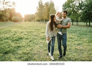 Happy mother, father hug baby son walking in garden at sunset. Family spending time together outdoors. Child with parents happiness playing in green grass in park. Children's day. Friendly family. - Powered by Shutterstock