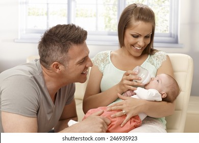 Happy mother and father smiling, looking at baby girl while feeding from bottle. - Powered by Shutterstock