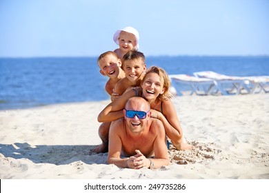 Happy Mother And Father With Three Children Lying On The Sunny Beach.