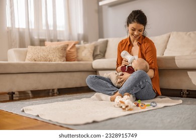 Happy mother is feeding her baby girl at home. Woman feeding newborn with formula in a bottle. - Powered by Shutterstock