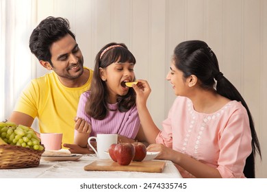 A HAPPY MOTHER FEEDING HER DAUGHTER WITH HUSBAND SITTING NEAR
 - Powered by Shutterstock