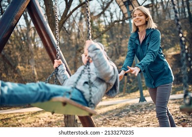 Happy mother having fun with her small daughter while pushing her on a swing in nature. - Powered by Shutterstock