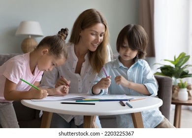 Happy mother helping cute little sibling kids to draw in colorful pencils in paper album  sitting at small table in living room  enjoying learning creative process  playtime  family leisure
