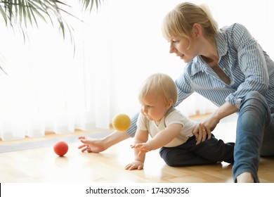 Happy Mother And Her 1 Year Old Son Playing With Small Ball At Home.