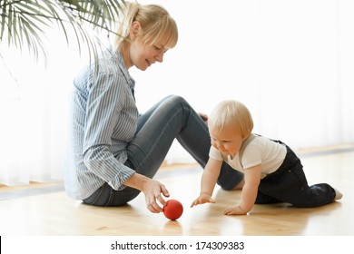 Happy Mother And Her 1 Year Old Son Playing With Small Ball At Home.