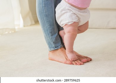 Happy Mother With Her Baby Girl Learn To Walk At Home In The Living Room