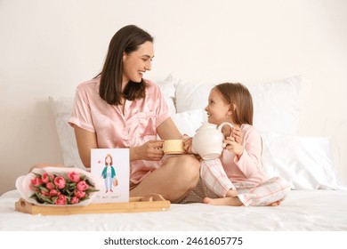 Happy mother with her cute little daughter pouring tea in bedroom - Powered by Shutterstock