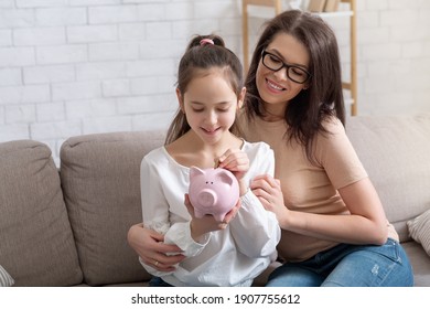 Happy Mother And Her Cute Teen Daughter Putting Coin Into Piggybank, Saving Money At Home, Copy Space. Family Budget, Financial Education For Children, Investments Concept