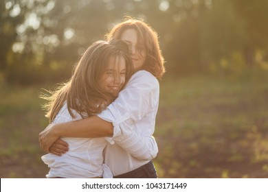 Happy Mother With Her Daughter Hugging A Teenager In The Summer In The Setting Sun