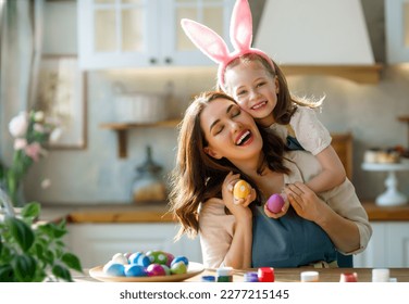 Happy mother and her daughter wearing aprons holding painted colorful eggs while decorating them with food dyes in cozy kitchen at home. Easter craft activities for families. - Powered by Shutterstock