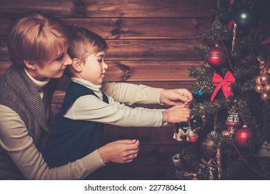 Happy mother and her lIttle boy decorating christmas tree in wooden house interior 