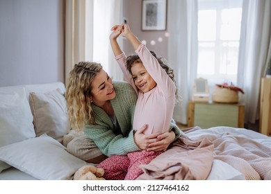 Happy mother hodling her little daughter stretching in bed when waking up in morning.