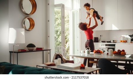 Happy Mother Holding Adorable Baby Boy, Playing, Having Fun at Modern Home Living Room. Black Female Lifting Up and Throwing Toddler Child Up in the Air. Concept of Childhood, New Life, Parenthood. - Powered by Shutterstock