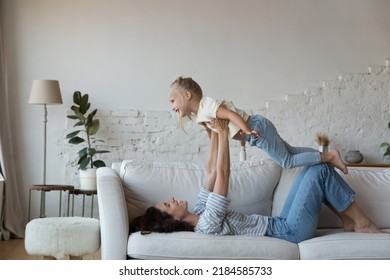 Happy Mother Holding Excited Kid On Outstretched Arms, Lifting Child Up In Air, Playing Flying Airplane With Daughter, Doing Yoga Exercise At Home, Having Fun, Enjoying Sportive Entertainment