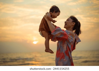 happy mother holding and lifting with her toddler baby girl on the sea beach at sunset - Powered by Shutterstock